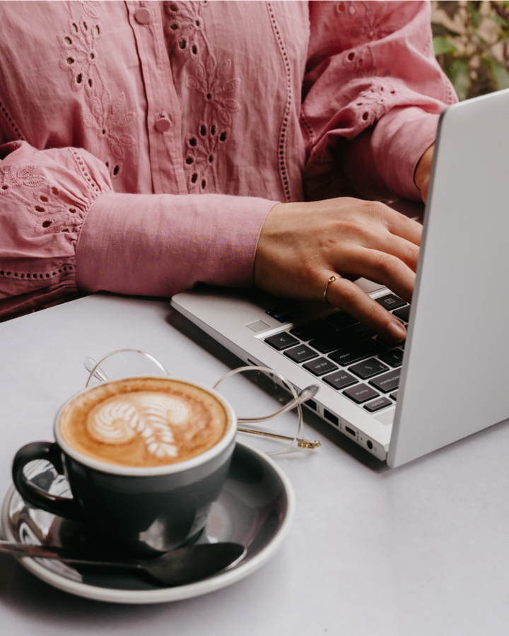 woman typing on laptop with a coffee